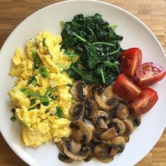 scrambled eggs, spinach, tomatoes and mushrooms on a white plate with red peppers