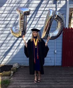 a woman in graduation gown and cap holding up two large silver balloons with the number 50 on them