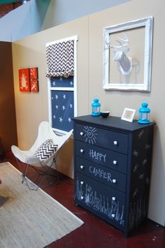 a room with a chalkboard on the wall next to a black dresser and chair