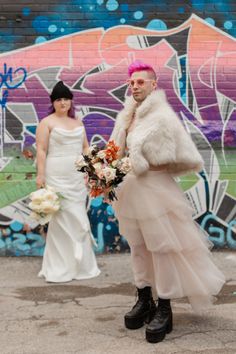 a man and woman standing next to each other in front of a wall with graffiti