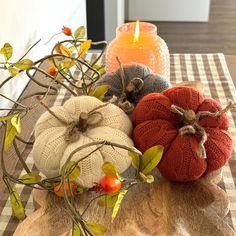 three knit pumpkins sitting on top of a table next to a candle and some branches