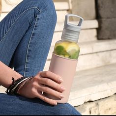 a woman sitting on the steps holding a pink water bottle with lime slices in it