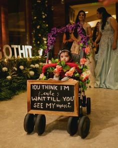 a small child in a wagon with flowers on it and a sign that says you think i'm quite want to see my mom