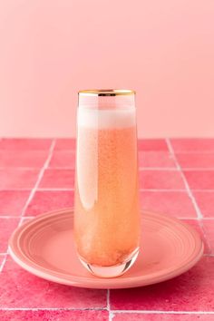 a glass filled with liquid sitting on top of a pink tile floor next to a plate