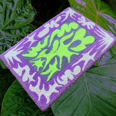 a green and purple flowered towel sitting on top of a lush green leafy plant