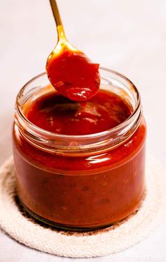 a spoon full of ketchup on top of a glass jar filled with sauce