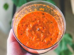 a hand holding a small glass filled with red sauce