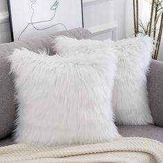 two white fluffy pillows sitting on top of a gray couch next to a framed drawing