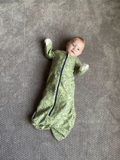 a baby laying on the floor wearing a green outfit