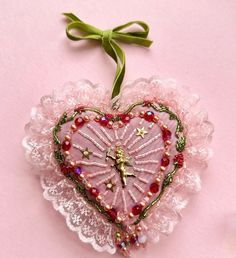 a pink heart shaped ornament hanging from a green ribbon on a pink background