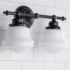 two light fixtures mounted on the wall in a bathroom with white tile and black accents