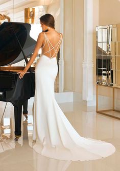 a woman standing in front of a piano wearing a white dress with open back and straps