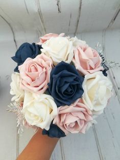 a bridal bouquet with blue and pink flowers on it's arm, in front of a white wooden background