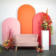 a pink couch sitting in front of a colorful wall with flowers and vases next to it