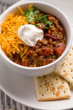 a white bowl filled with chili and cheese next to crackers