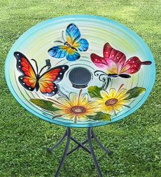 a glass birdbath sitting on top of a green grass covered field with butterflies painted on it