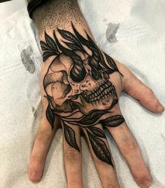 a person's hand with a skull and leaves tattoo on the middle of it