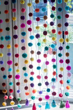 multicolored pom - poms hanging from curtains in front of a window