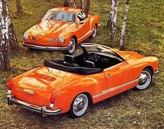 an orange convertible car parked in the woods next to another red convertible car with its top down