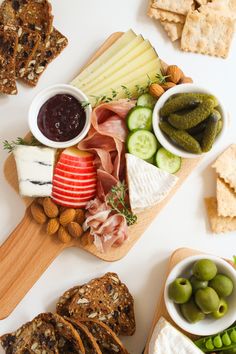 an assortment of cheeses, crackers, olives, and pickles on a cutting board