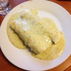 a white plate topped with meat covered in gravy next to a glass of water