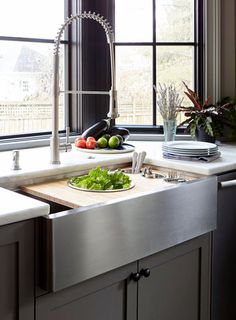 a stainless steel kitchen sink with cutting board and vegetables on the counter in front of it