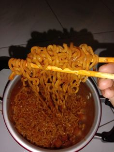 someone is holding chopsticks over a bowl of noodles