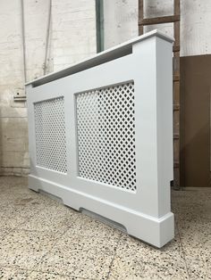 a large white radiator cover sitting on top of a floor next to a brick wall