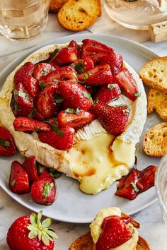 a white plate topped with cheese and strawberries next to crackers on a table