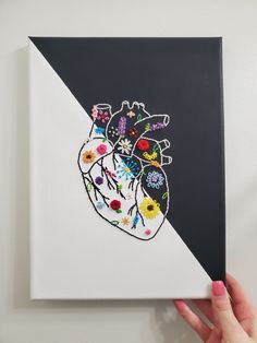 a hand holding up a piece of art with flowers on it and a heart painted on the side