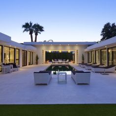 an outdoor living area with couches and tables next to a swimming pool at dusk