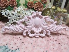 some pink and white decorative items sitting on a lace covered tablecloth with roses in the background