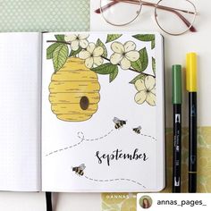 an open notebook with a beehive and flowers on it next to some pens