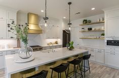 a large kitchen with white cabinets and gold hood lights hanging from the ceiling, surrounded by black bar stools