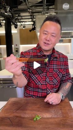 a man is holding a knife and chopping green vegetables on a cutting board in front of him