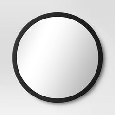 a round mirror on the wall with black frame and white backround, in front of a gray background