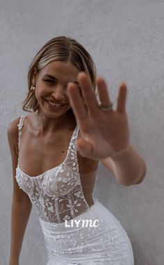 a woman in a white dress is smiling and waving her hand up to the camera