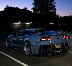 a blue sports car parked in a parking lot at night with its lights turned on