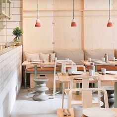 tables and chairs in a restaurant with white tiles on the walls, wood flooring and pink pendant lights hanging from the ceiling