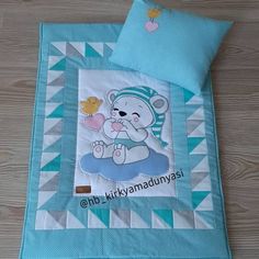 a blue and white teddy bear quilted on top of a wooden floor next to a pillow