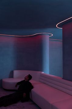 a man sitting on a white couch in a room with curved walls and purple lighting