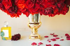 a vase filled with red roses next to a bottle of perfume and petals on the ground