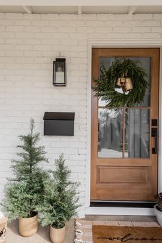 two potted plants sitting on the front porch next to a door with a wreath