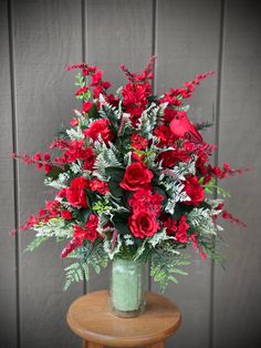 a vase filled with red flowers sitting on top of a wooden table next to a wall