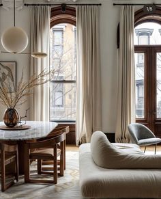 a living room filled with furniture next to two large windows covered in curtains and drapes