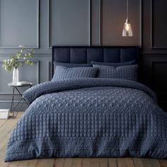 a bed with blue bedspread and pillows in a dark room next to a table