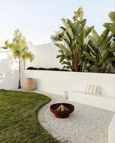 a white fenced in area with grass and plants next to it, including a fire pit