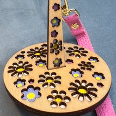 a wooden clock with flowers on it and a pink leash attached to the back of it