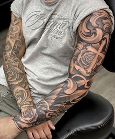 a man with a cross tattoo on his arm sitting in front of a black chair