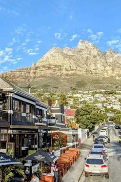 cars parked on the side of a road next to buildings and mountains in the background